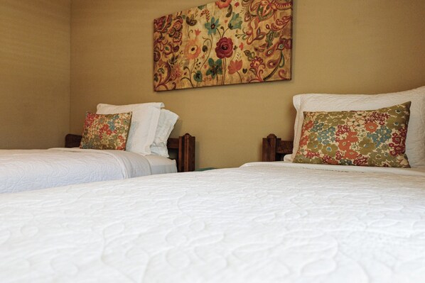 A hotel room with two beds, each with white bedding and floral-patterned pillows.