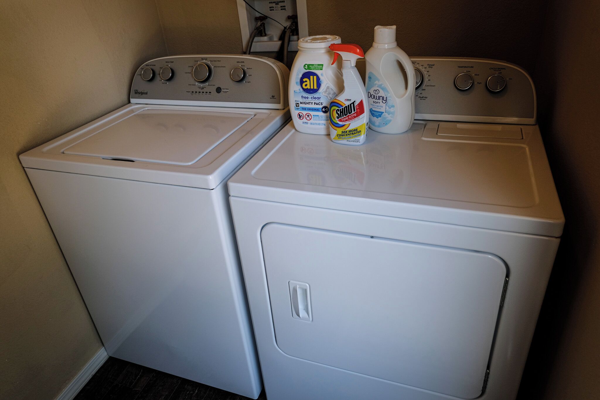 A front-loading washer and dryer in a laundry room with detergent bottles on top.
