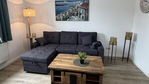 A living room with a sectional sofa, a coffee table with a plant, a painting on the wall, a clock, and two floor lamps.
