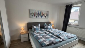 A bedroom with a bed, nightstands, a lamp, a painting, and a window with curtains.