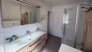 A modern bathroom with a large mirror, a sink with a wooden vanity, a glass shower enclosure, and a toilet.