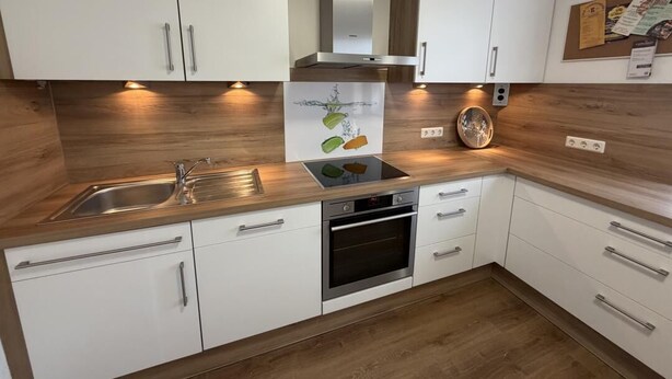 A modern kitchen with white cabinets, stainless steel appliances, and wooden countertops.