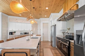 Cocina moderna con una isla central, electrodomésticos de acero inoxidable y techo de madera.