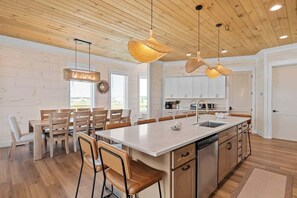A modern kitchen with wooden cabinets, a central island, and pendant lighting. - Private Pool | Gulf Views | Beachfront Access (Gulf Shores)