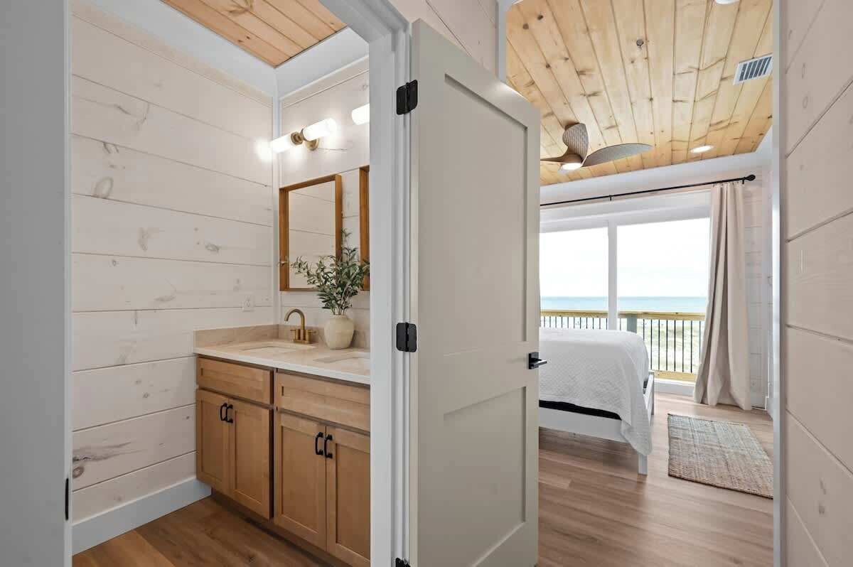 Une chambre avec un plafond en bois, une grande fenêtre avec des rideaux, un lit et une vue sur la mer.