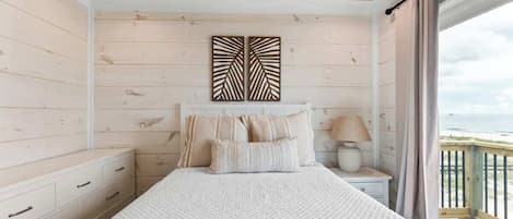 A bedroom with a bed, bedside table, lamp, and a view of the sea.