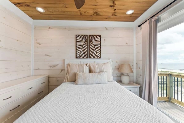 Un dormitorio con cama, mesita de noche, lámpara y vista al mar.