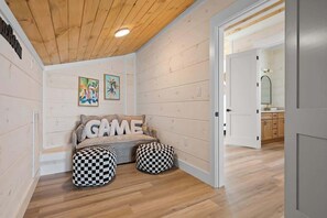 A cozy room with a wooden ceiling, a sofa with 'GAME' cushions, and checkered ottomans. - 8-Bedroom Beachfront Home in Gulf Shores with Private Pool & Arcade (Gulf Shores)