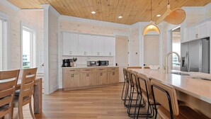A modern kitchen with wooden cabinets, a central island with bar stools, and a stainless steel refrigerator. - Private Pool | Gulf Views | Beachfront Access (Gulf Shores)