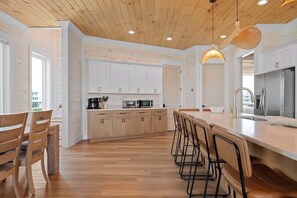 A modern kitchen with wooden cabinets, a central island with bar stools, and a stainless steel refrigerator. - Private Pool | Gulf Views | Beachfront Access (Gulf Shores)