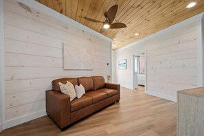A room with a wooden ceiling, a brown leather sofa, and a white wall with a painting. - 8-Bedroom Beachfront Home in Gulf Shores with Private Pool & Arcade (Gulf Shores)
