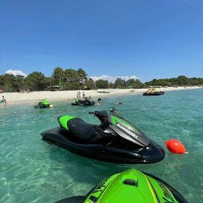 Ein Jetski am Strand mit klarem Wasser, sandigem Ufer und Bäumen im Hintergrund.