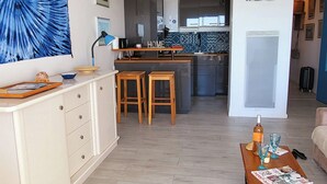 A modern kitchen with a central island, a dining area with stools, a white cabinet with drawers, and a 'Welcome' sign. - Le plein Sud entre Plage 🏖️ et Commerces (Le Grau-du-Roi)