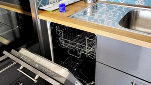 A kitchen with a dishwasher, oven, and a blue patterned backsplash. - Le plein Sud entre Plage 🏖️ et Commerces (Le Grau-du-Roi)