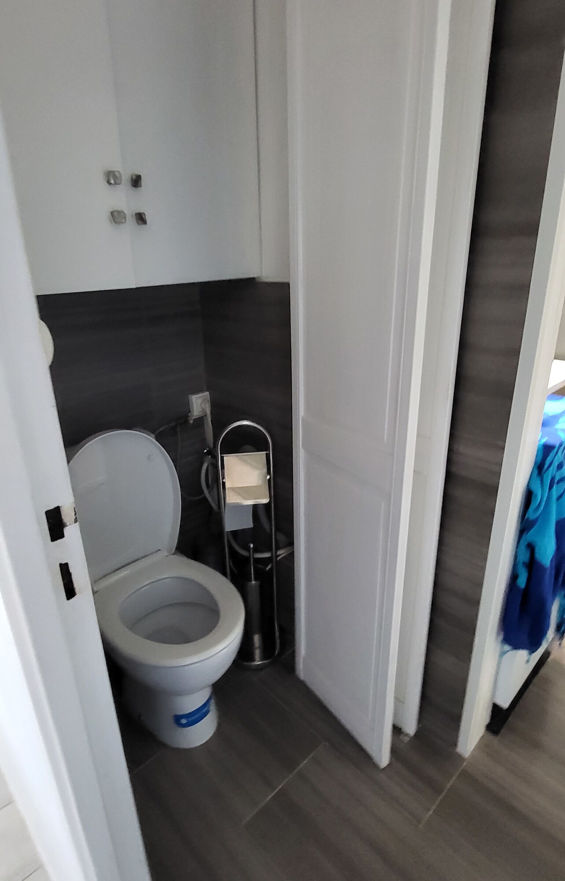A compact bathroom with a toilet, a shelf, and a towel rack.