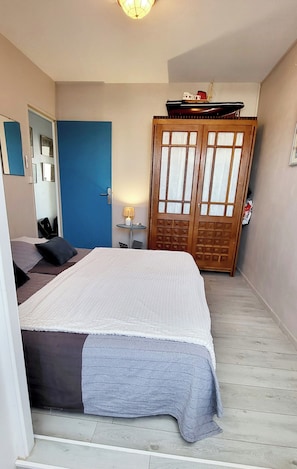 Une chambre à coucher avec un lit, une porte bleue, une armoire en bois et une petite table avec une lampe.