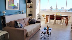 A living room with a sofa, coffee table, and a dining area with chairs and a table. - Le plein Sud entre Plage 🏖️ et Commerces (Le Grau-du-Roi)