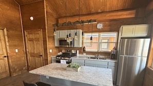 Une cuisine moderne dotée d’un grand îlot central, de tabourets de bar, d’appareils électroménagers en acier inoxydable et de panneaux muraux en bois.