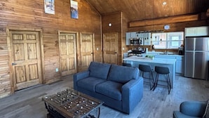 Un vaste espace de vie doté d’un plafond en bois, d’un canapé, d’une table basse et d’une cuisine en arrière-plan.