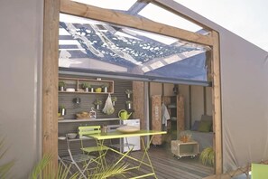 Ein moderner Außenbereich mit Küche, einem Holzboden, einem grünen Tisch und verschiedenen Küchengeräten.