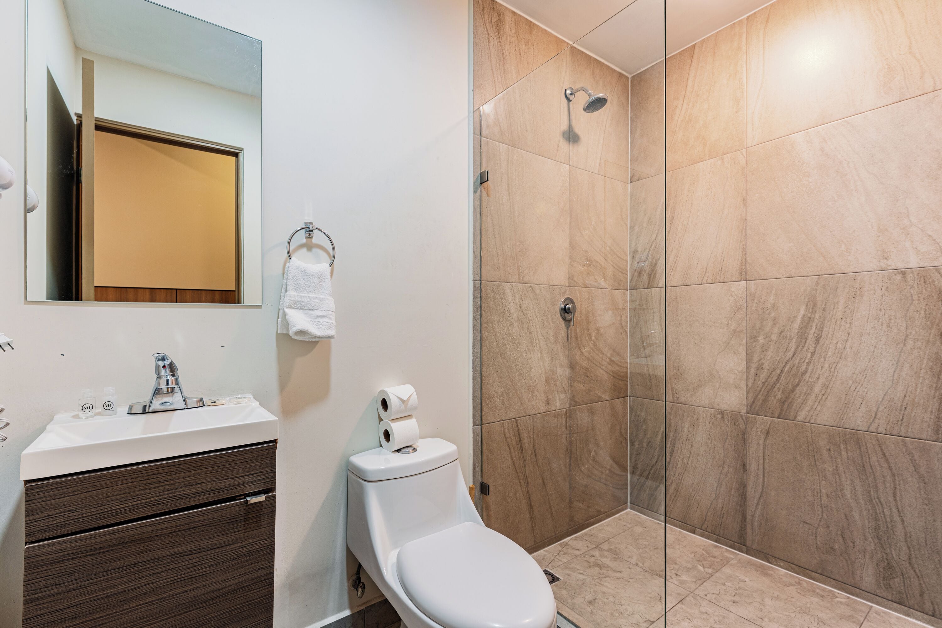 A bathroom with a toilet, sink, mirror, and shower area.