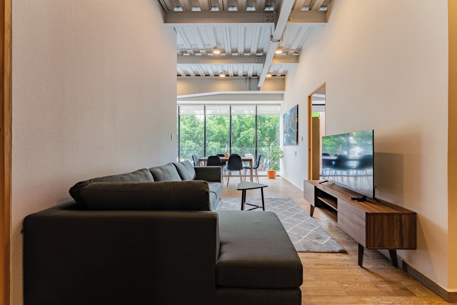 A modern living room with a sectional sofa, a flat-screen TV, and a dining area with chairs and a table.
