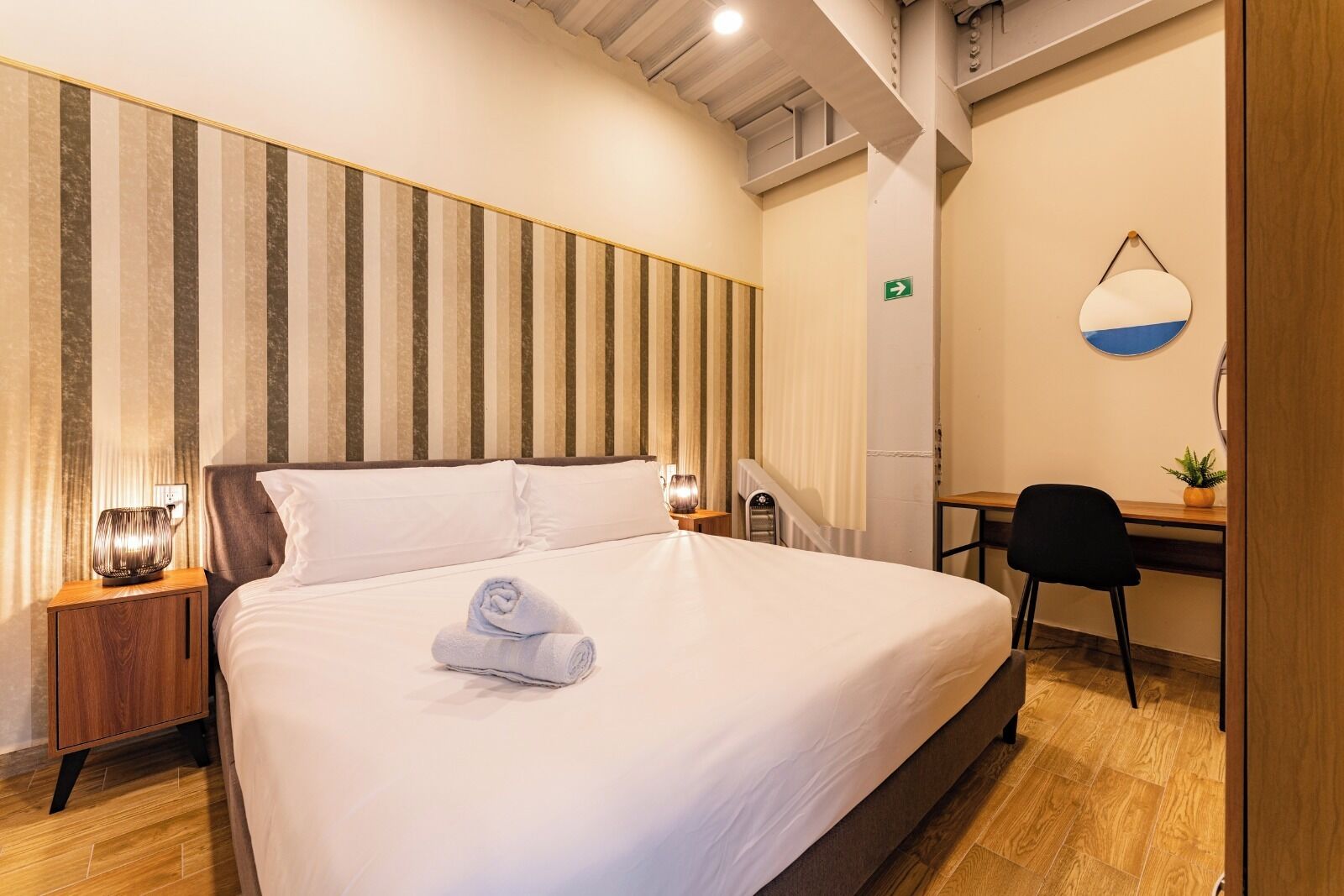 A hotel room with a large bed, a desk, a chair, and a wall with vertical stripes.