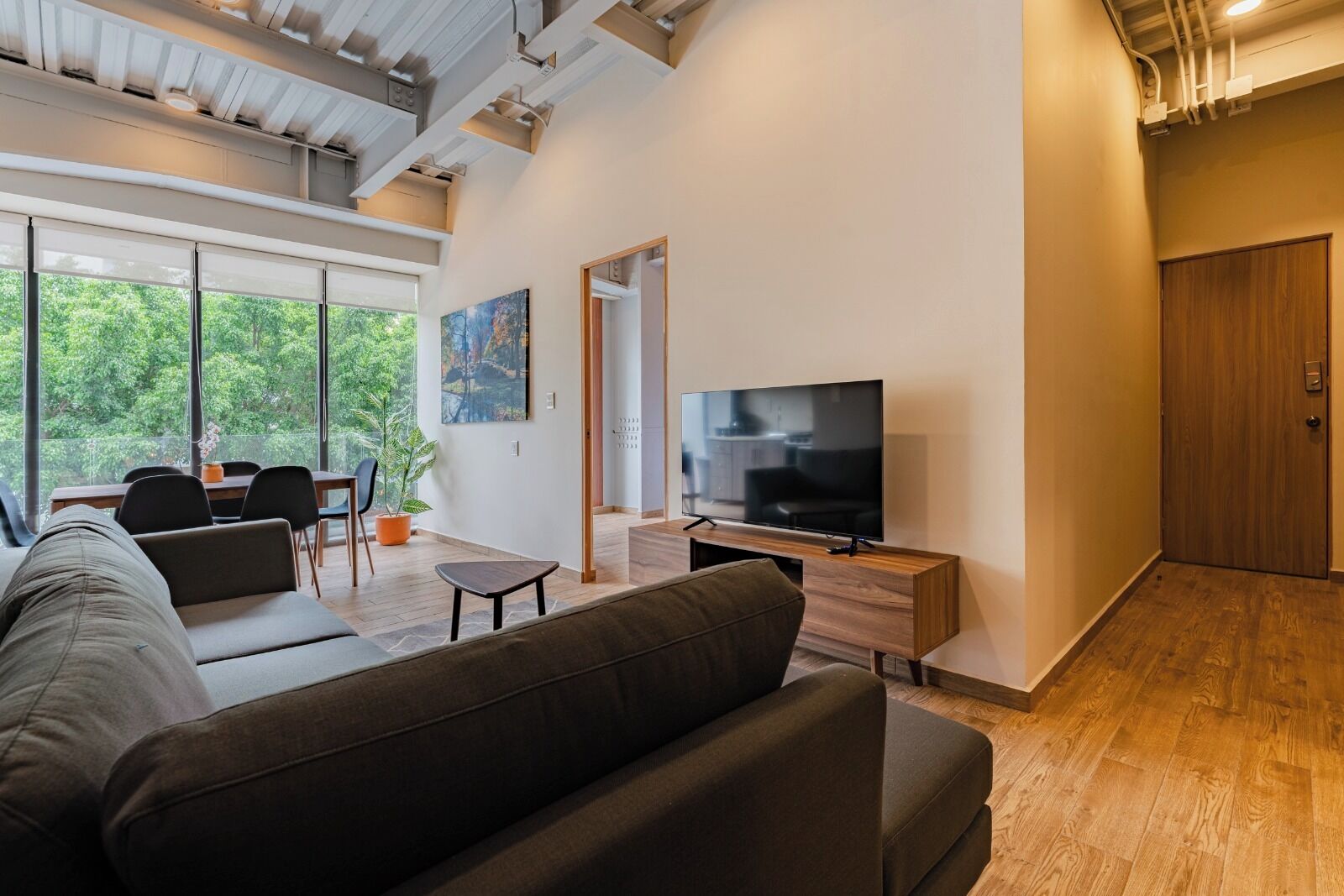 Un salon moderne avec un canapé, un téléviseur, un coin repas et de grandes fenêtres.