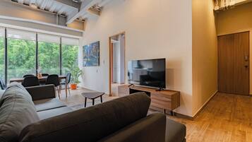 Un salon moderne avec un canapé, un téléviseur, un coin repas et de grandes fenêtres.