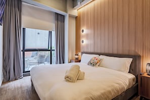 A hotel room with a large bed, a window with curtains, a wooden wall panel, and a small table with a lamp. - Casa by Frida Kahlo (Mexico City)