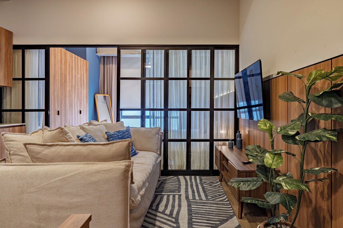 Una sala de estar moderna con un sofá, una mesa de centro, un televisor y un ventanal con cortinas.