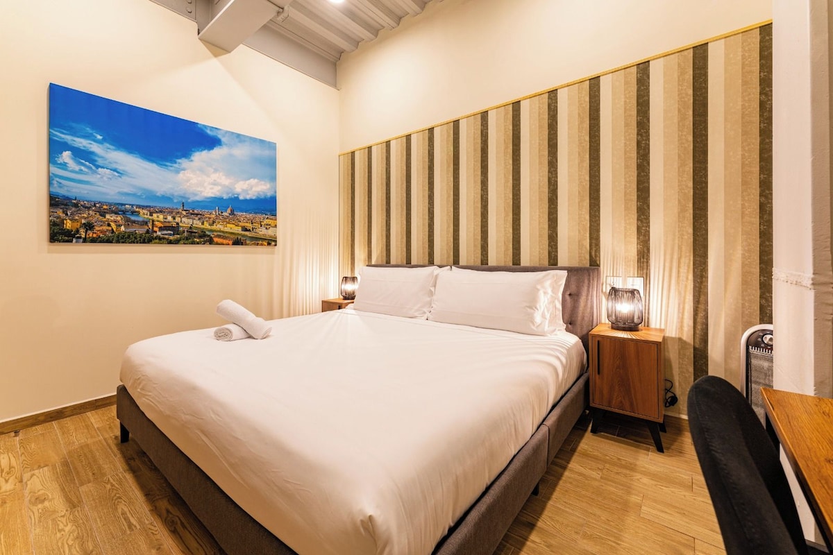 A neatly made bed with white linens, a cityscape painting on the wall, and a striped wall panel.