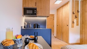 Une cuisine compacte équipée d’un four à micro-ondes, d’une machine à café et de divers articles pour le petit-déjeuner, le tout disposé sur le comptoir.