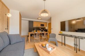 Ein modernes Wohnzimmer mit einer Couch, einem Esstisch mit Stühlen, einer Küchenzeile inklusive Schränken und Geräten sowie einem an der Wand befestigten Fernseher.