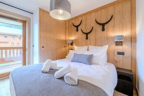 Ein modernes Hotelzimmer mit einer Holzvertäfelung, einem Bett mit weißer Bettwäsche, zwei Wandleuchten und einem Fenster mit Blick auf Gebäude.