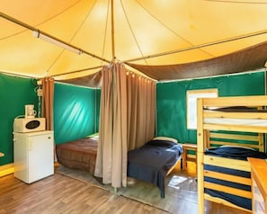 Ein Zelttraum mit einem Bett, einem kleinen Tisch, einer Mikrowelle und einem Etagenbett.