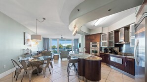 Una cocina moderna con una isla central, electrodomésticos de acero inoxidable y un comedor con mesa de vidrio y sillas metálicas.