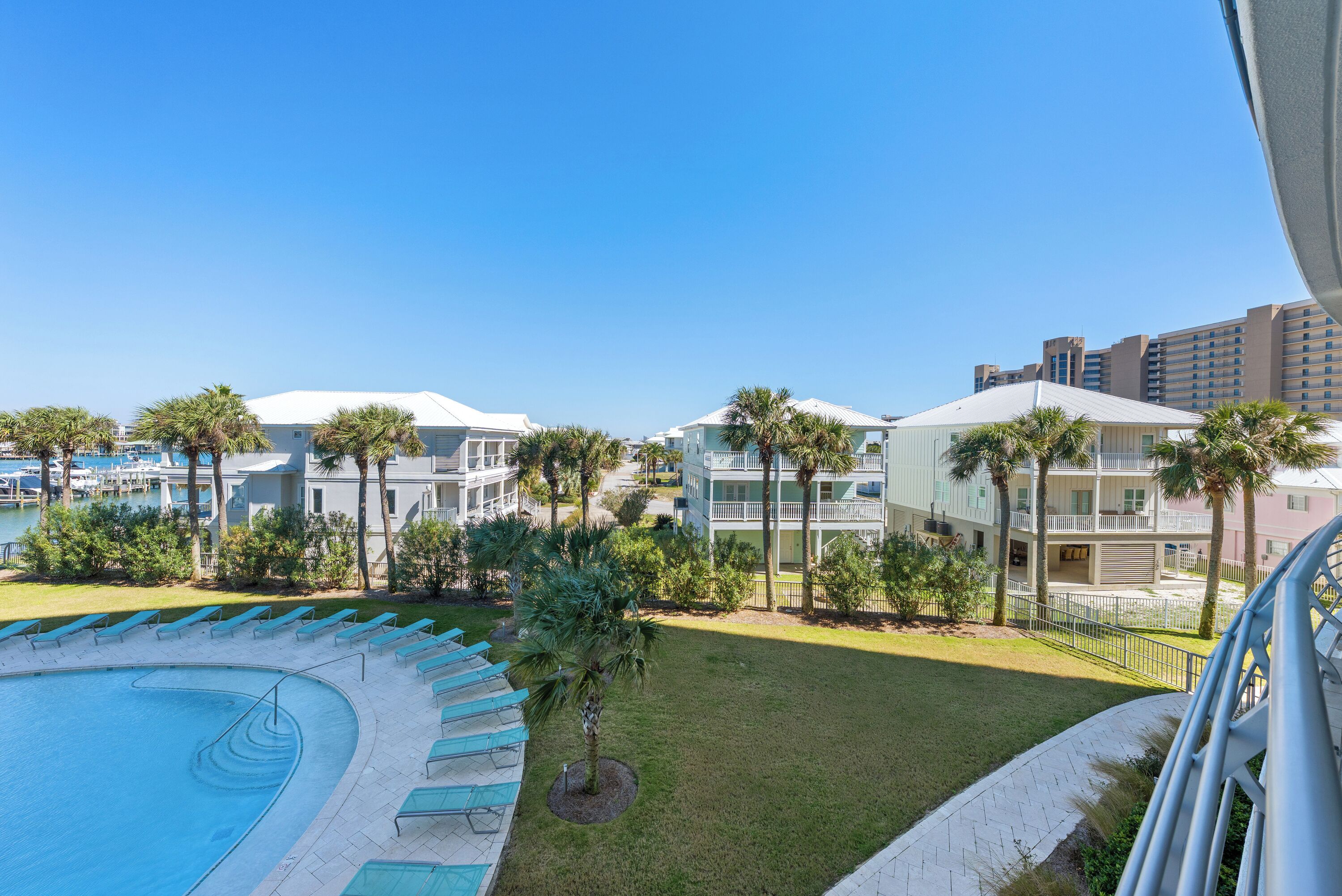 A pool with lounge chairs, a grassy area, and buildings with balconies.