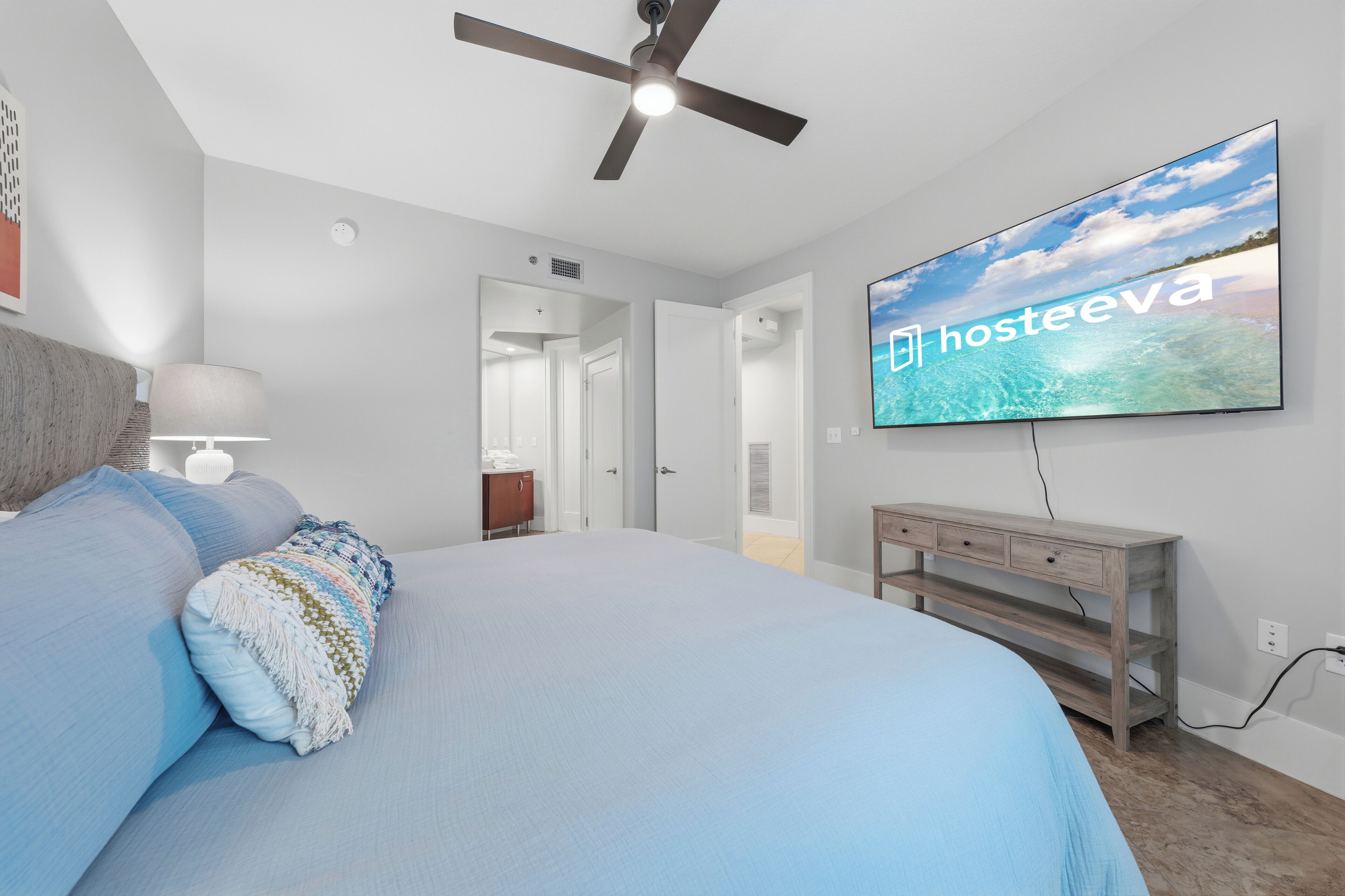Un dormitorio con cama, ventilador de techo, televisor y mesita de noche de madera.