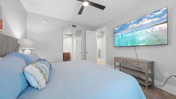 Un dormitorio con cama, ventilador de techo, televisor y mesita de noche de madera.