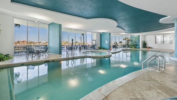 Una piscina interior con paredes de vidrio transparente, techo curvo y vistas de la ciudad.