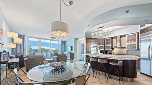 Una cocina moderna con una isla central, taburetes de bar y un comedor con mesa de vidrio y sillas.