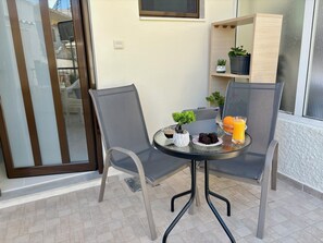 Ein kleiner Balkon mit zwei Stühlen, einem Tisch, einem Blumentopf, einem Glas Orangensaft und einer Kaffeetasse.