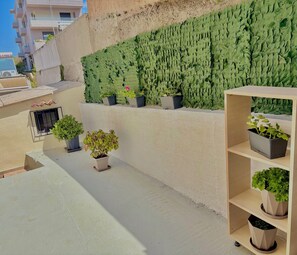 Eine Dachterrasse mit Kübelpflanzen, einer vertikalen Begrünung an der Wand und einem kleinen Fenster.