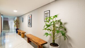 Un couloir avec un banc en bois, une plante en pot et des tableaux encadrés accrochés au mur.