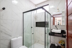 Um banheiro moderno com chuveiro em cabine de vidro, vaso sanitário branco, pia preta e parede revestida em mármore.