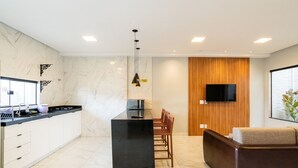 Une cuisine moderne avec un îlot central noir, des armoires blanches et un mur d’accent en bois.