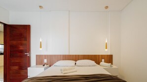 Une chambre d’hôtel moderne avec une tête de lit en bois, un grand lit avec du linge de lit blanc, deux tables de chevet et des lampes suspendues.