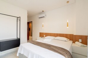 A hotel room with a bed, bedside tables, an air conditioning unit, and pendant lights.