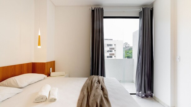 Une chambre d’hôtel avec un lit, une fenêtre avec des rideaux, une table de chevet et une lampe fixée au mur.